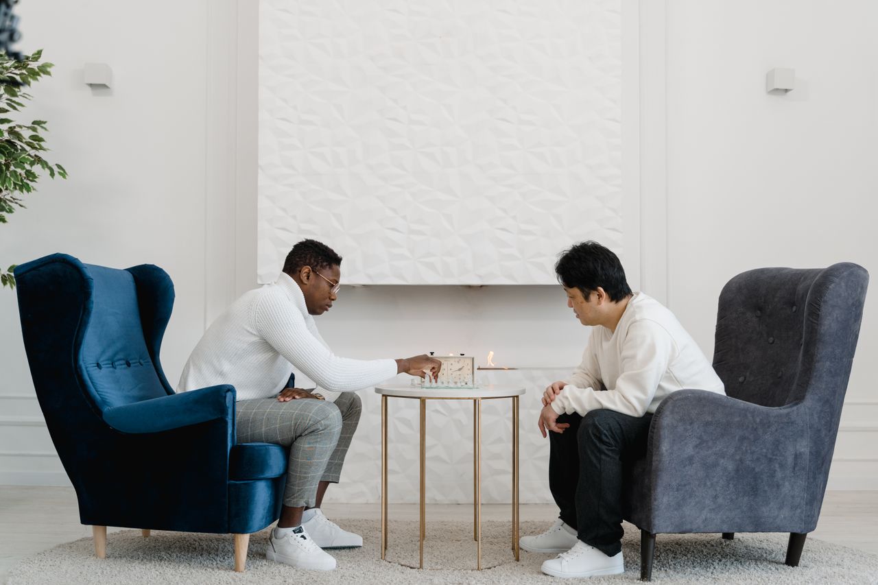 Two men deeply focused on a strategic board game indoors with elegant armchairs and a modern setting.